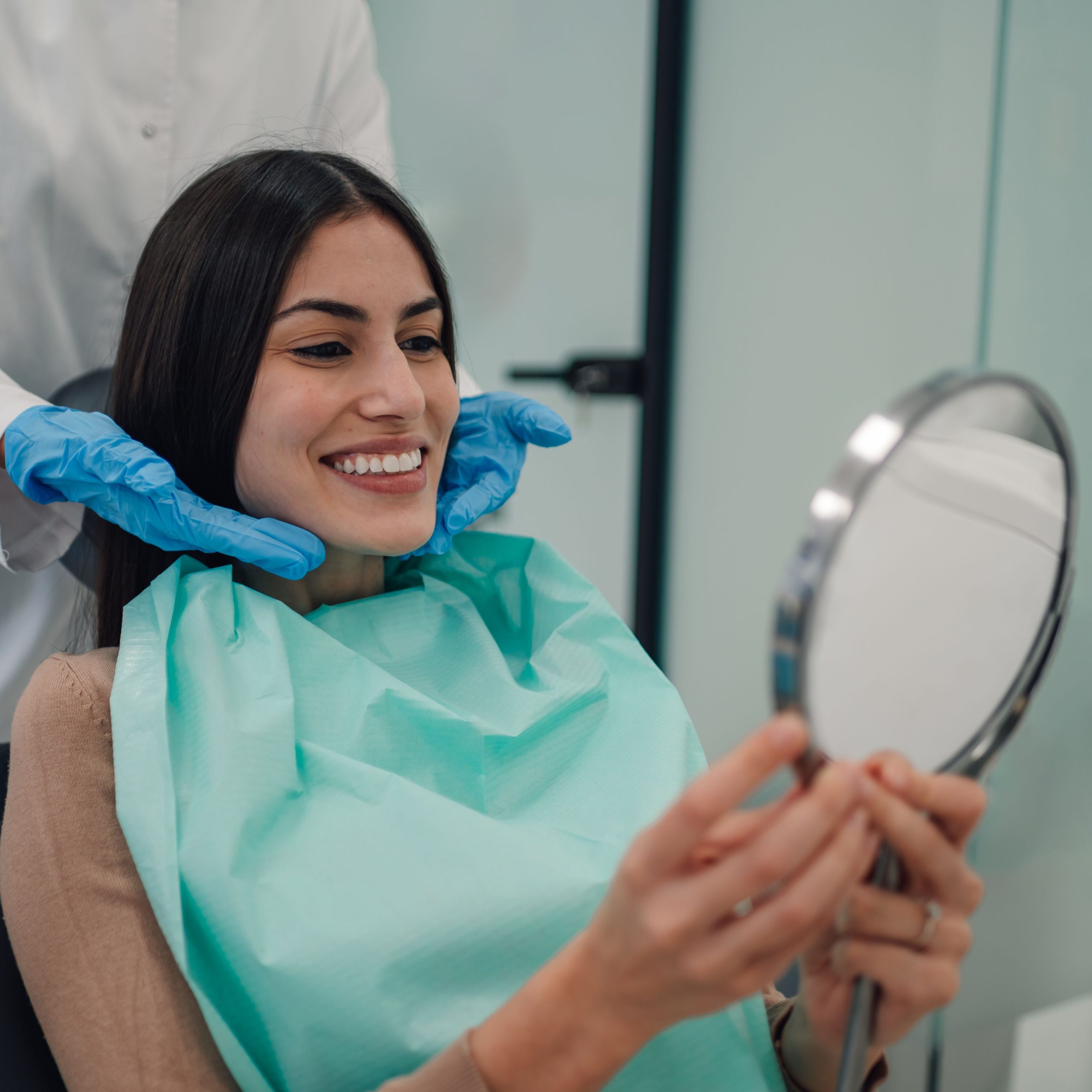 a female dentist wearing a medical mask and rubber gloves poses for the camera and folds her arms in her office