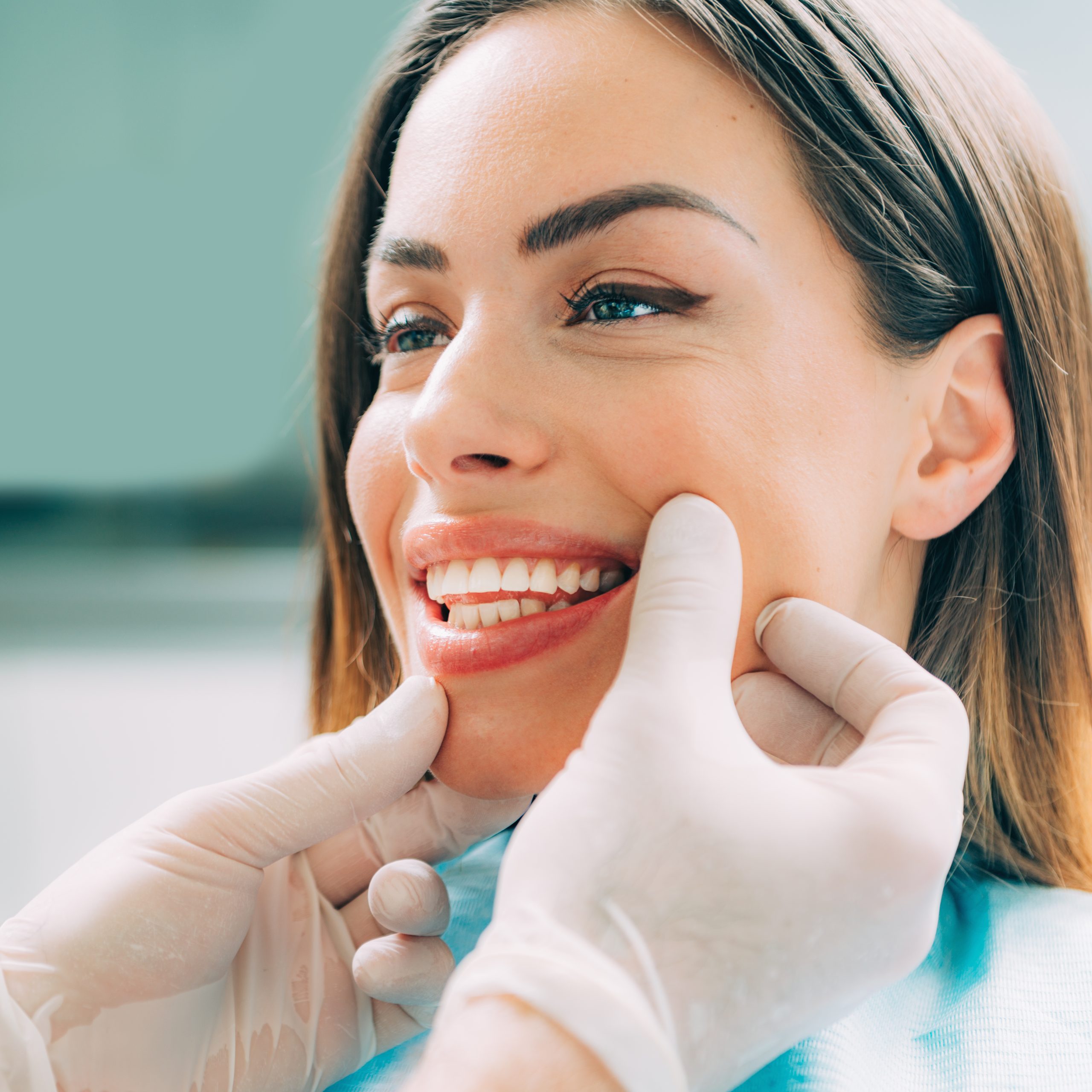 a female dentist wearing a medical mask and rubber gloves poses for the camera and folds her arms in her office