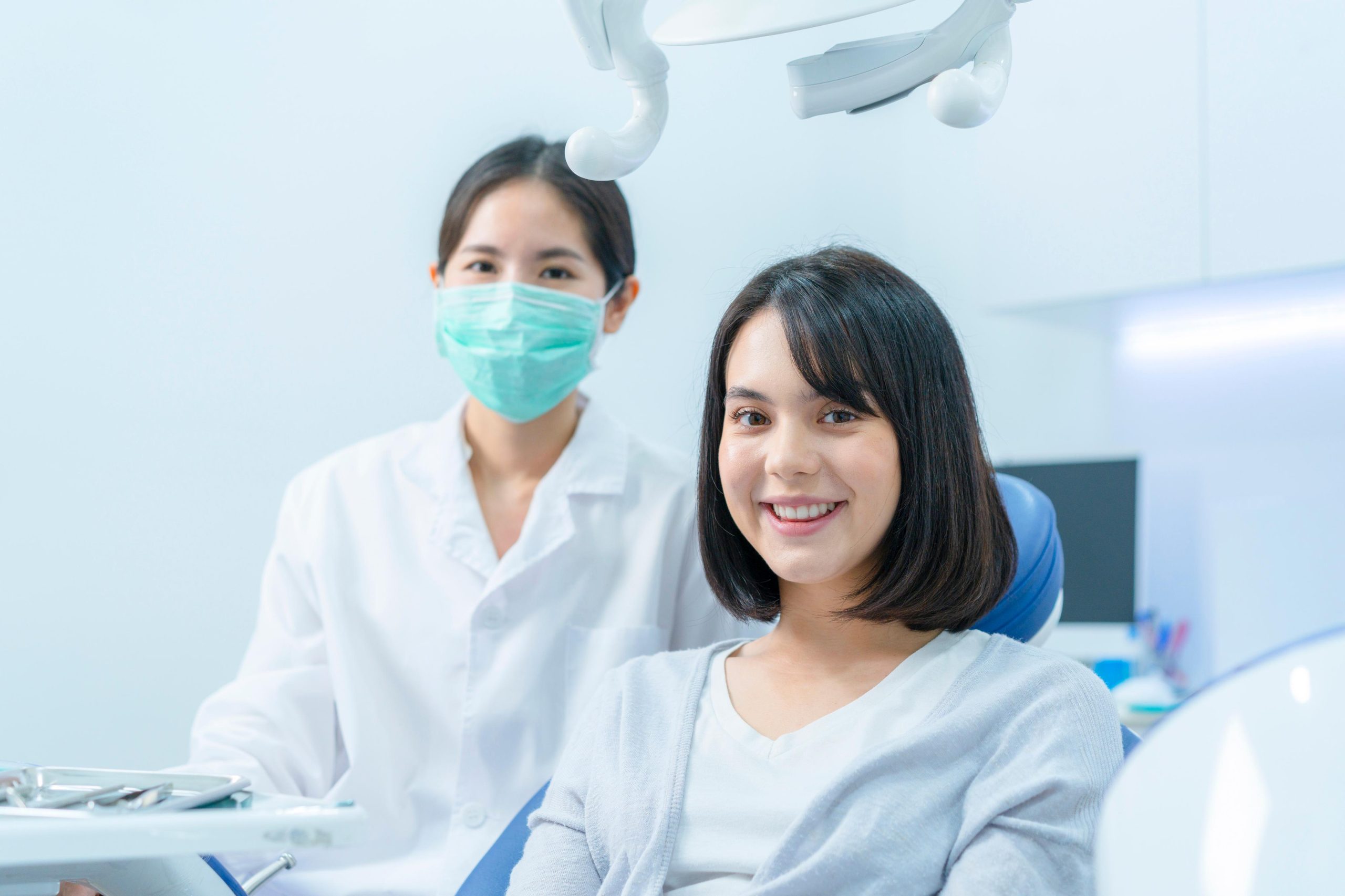 a female dentist wearing a medical mask and rubber gloves poses for the camera and folds her arms in her office